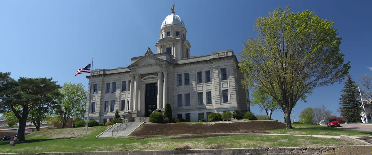 A large, historic building with a dome and columns, an American flag, and a well-maintained lawn.