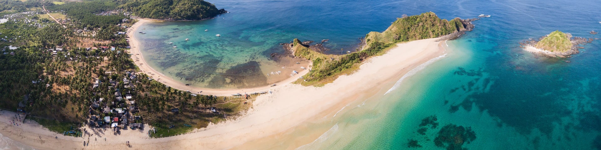 A coastal landscape with a sandy beach, clear turquoise waters, and lush green hills.