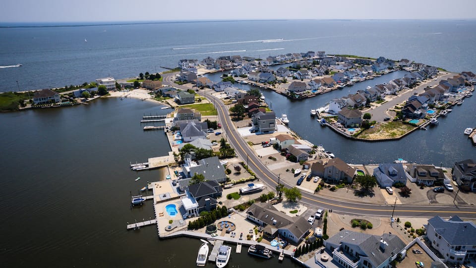 An aerial view of a coastal residential area with houses, a marina, and a road.