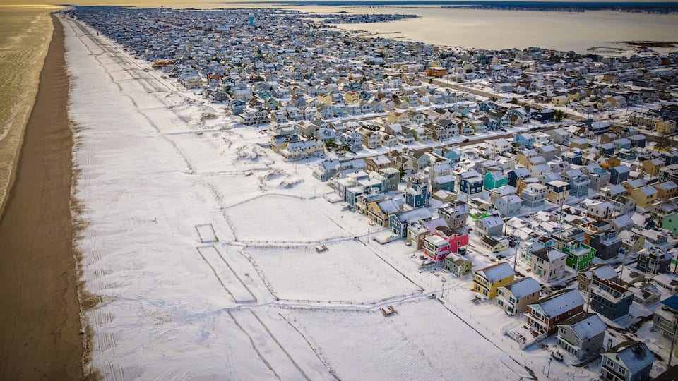 An aerial view of a coastal town with a beach on the left and densely packed houses on the right.