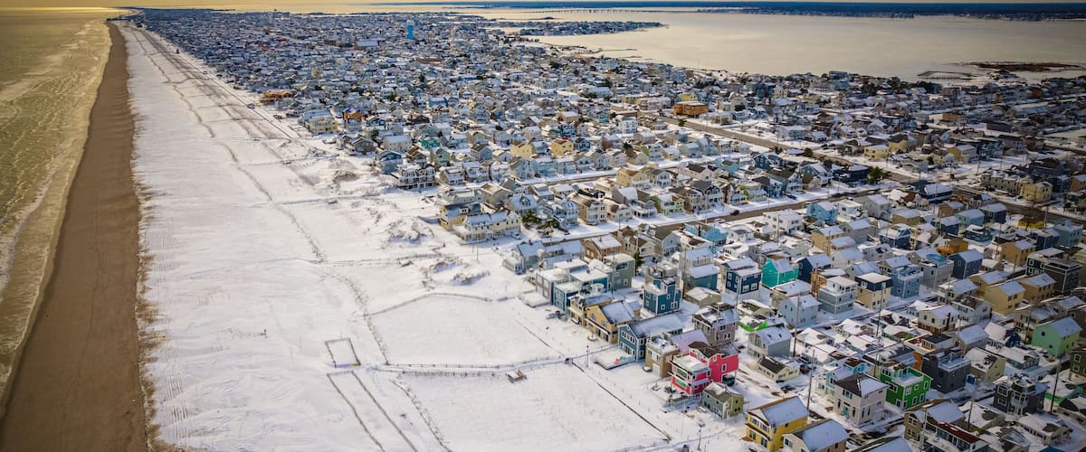 An aerial view of a coastal town with a beach on the left and densely packed houses on the right.