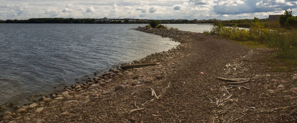 A lakeside with a rocky shore, calm water, and a cloudy sky.