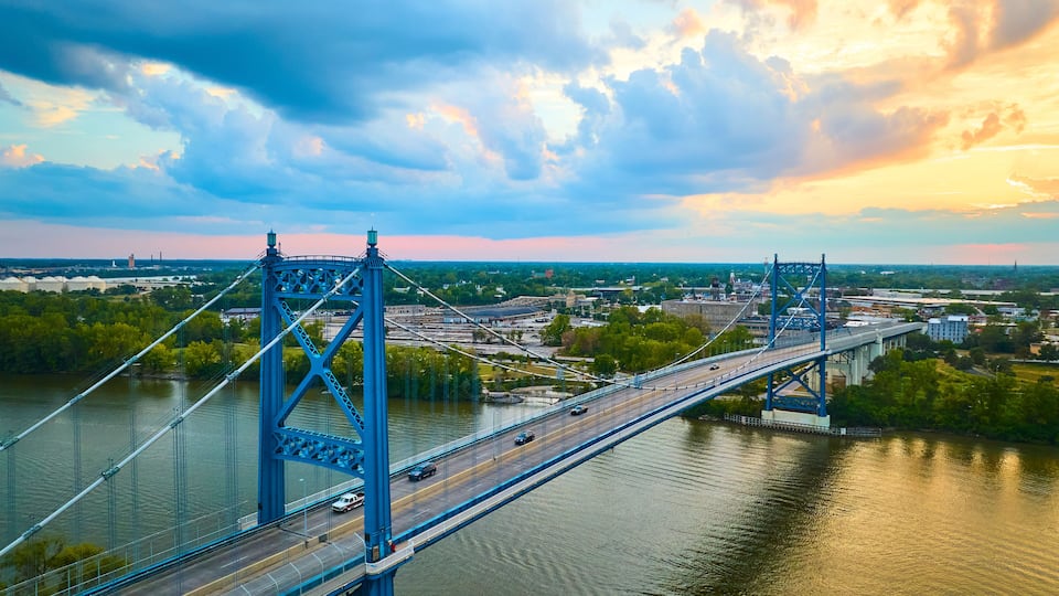 A blue bridge over a river with a cityscape in the background.