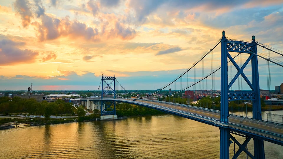 A suspension bridge over a river with a sunset sky.