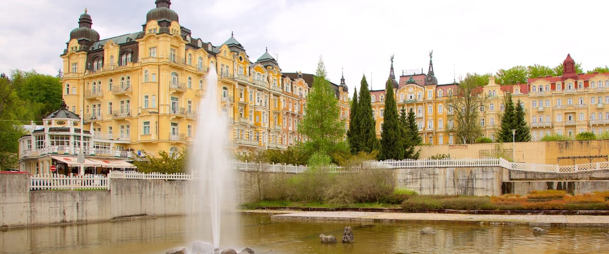 A historic yellow building with ornate architecture, a fountain, and a white picket fence.