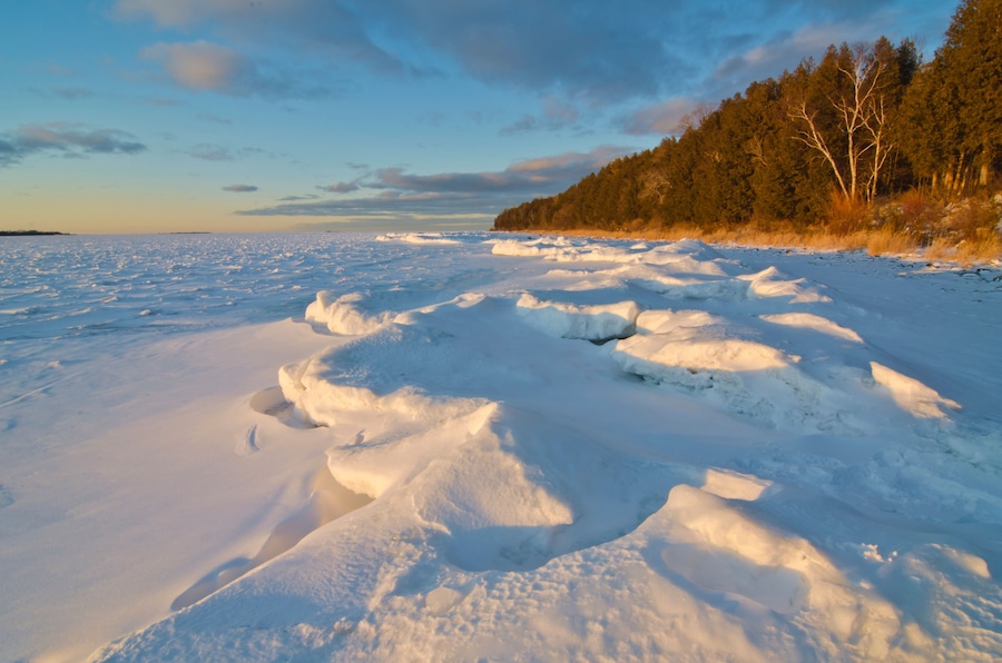A frozen landscape with snow-covered ground and a forest in the background.