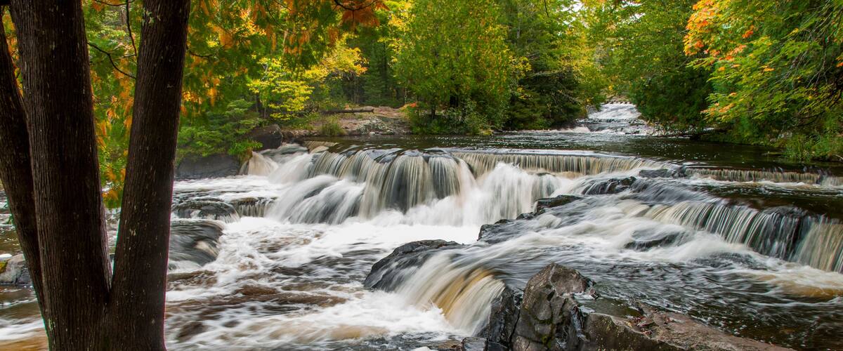 A waterfall cascading over rocks in a forested area with autumn foliage.