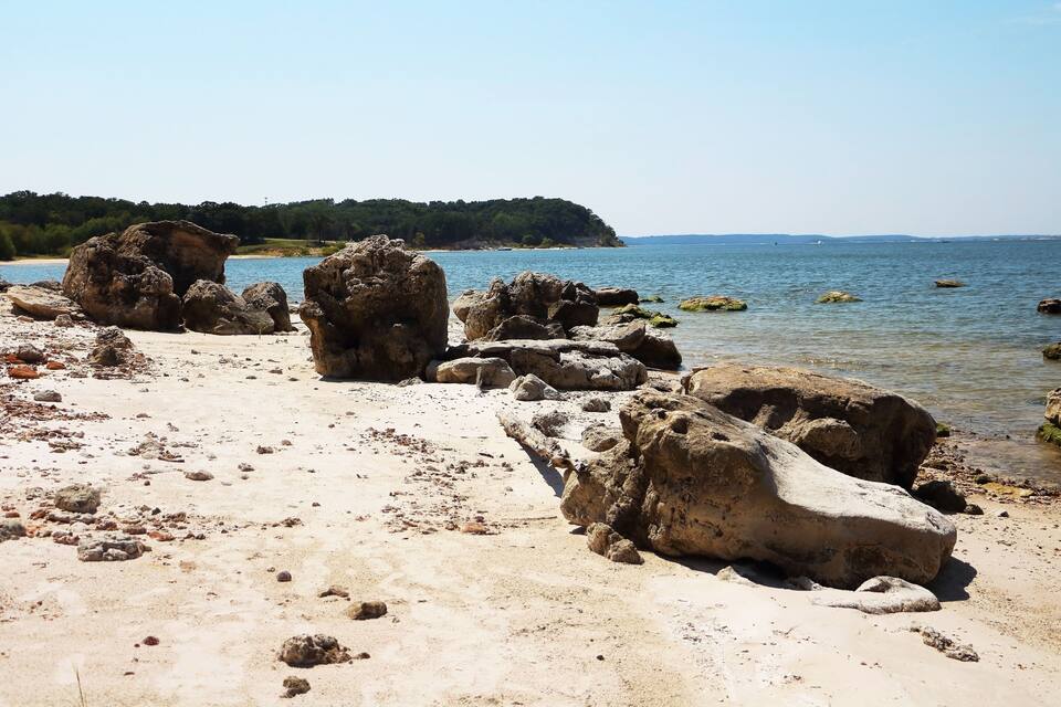 Un littoral rocheux, parsemé de gros blocs de pierre, et une colline boisée qui se dessine à l’horizon.