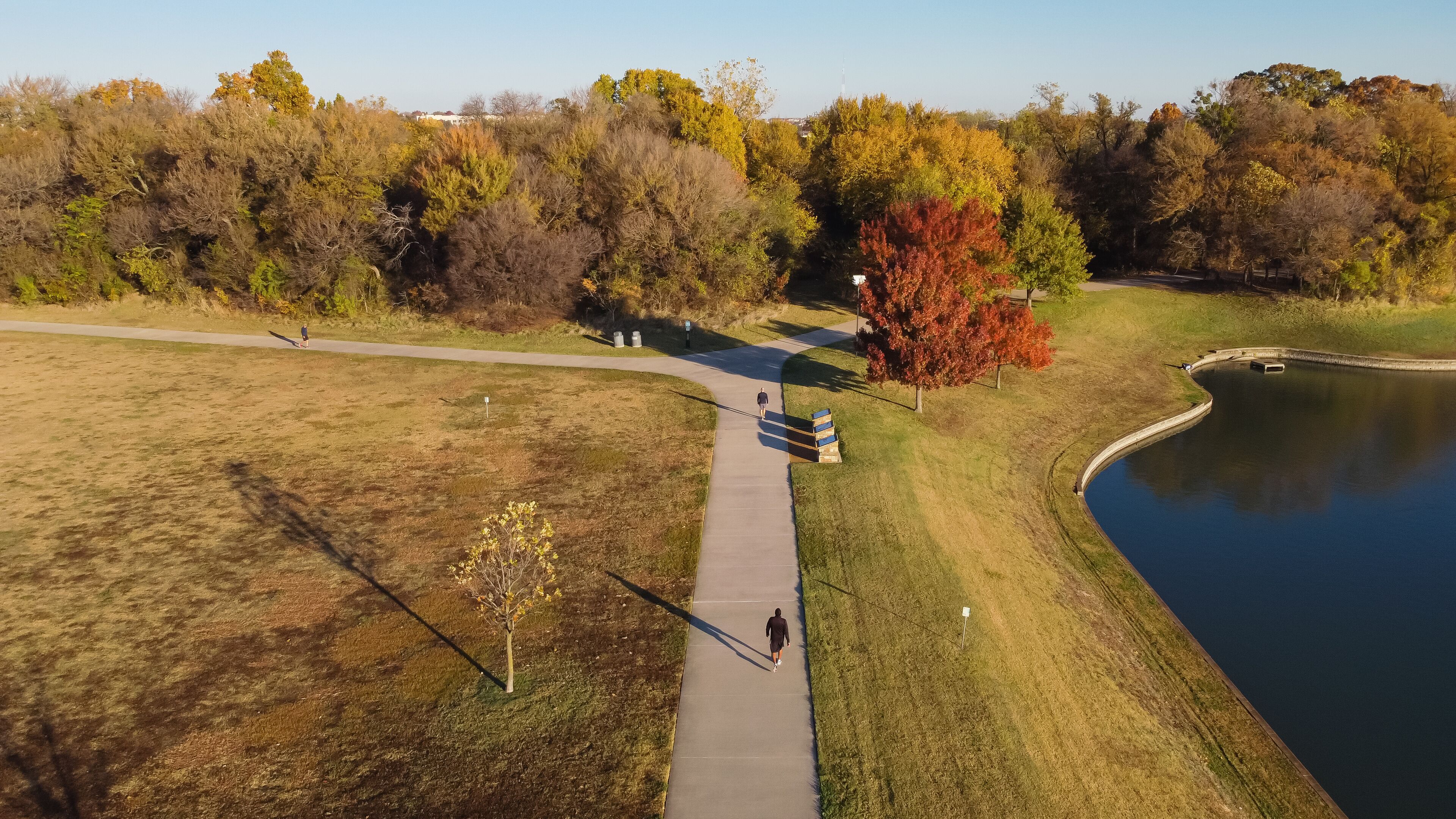 Aerial rear view of two men walking at lakeside park with colorful fall foliage and sunny blue sky near Dallas, Texas, USA