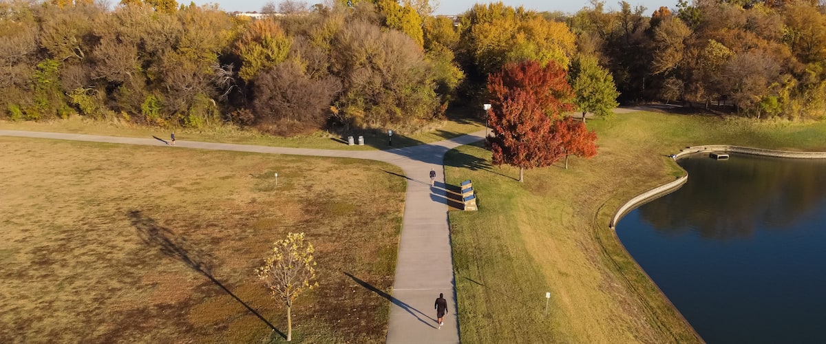 Aerial rear view of two men walking at lakeside park with colorful fall foliage and sunny blue sky near Dallas, Texas, USA