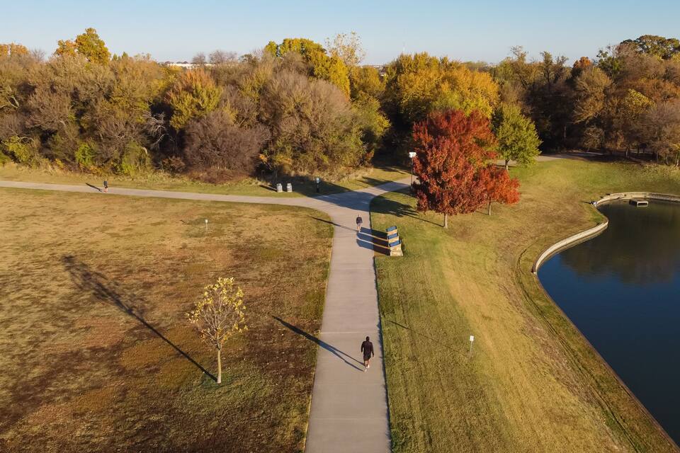 A park with a walking path, a pond, and autumn-colored trees.