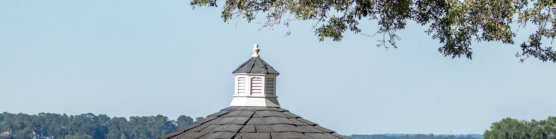 A white gazebo with a black roof by a lake.