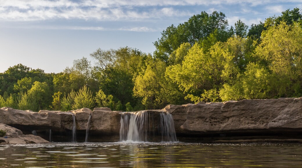 Waterfall at McKinney Falls State Park with large trees and blue sky background, Austin, Texas