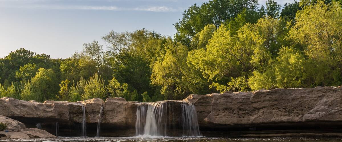Waterfall at McKinney Falls State Park with large trees and blue sky background, Austin, Texas