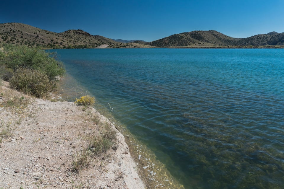 A clear lake with a rocky shore and distant hills.