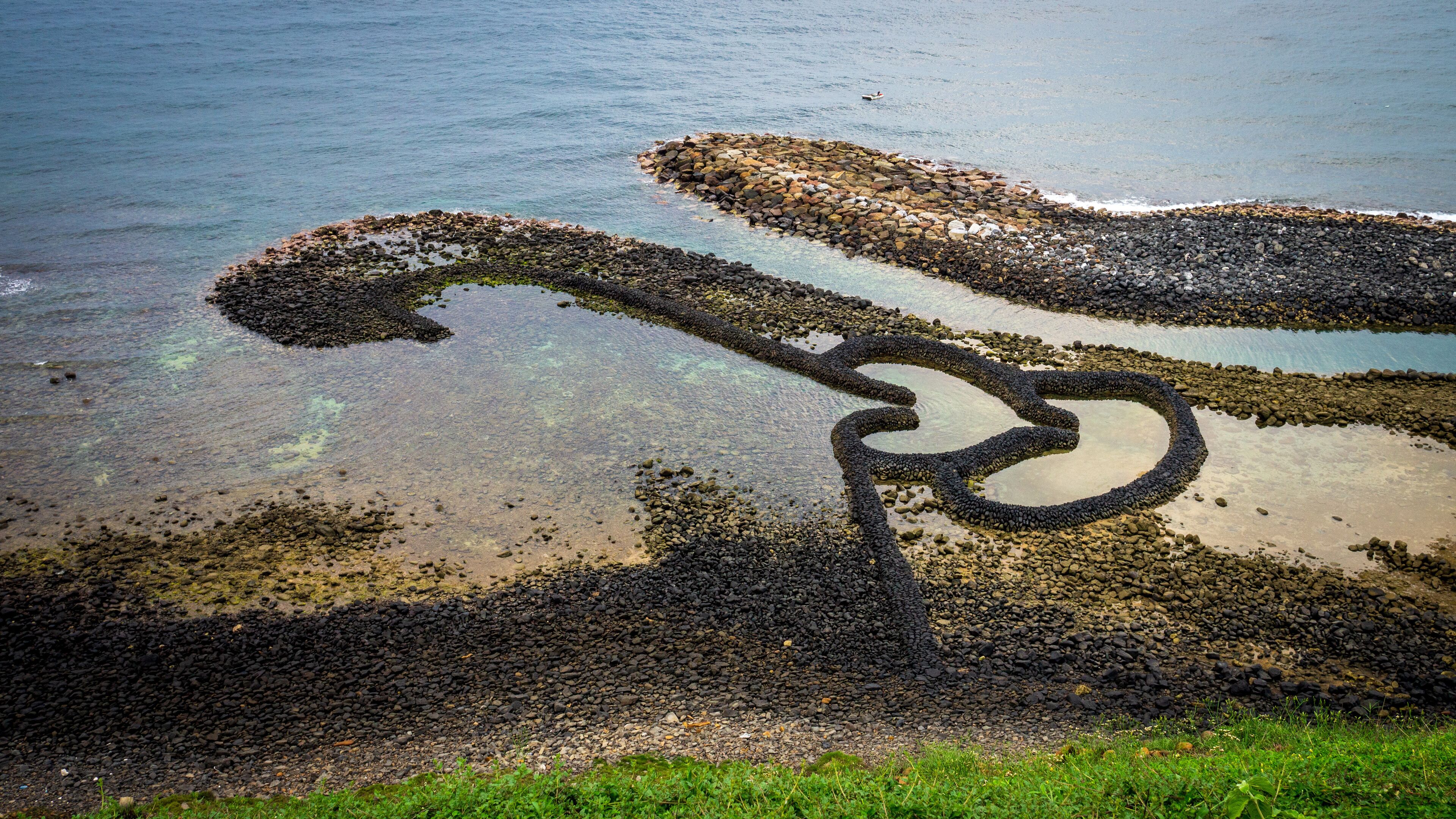 A rocky shoreline with clear water and a bicycle wheel-like formation.