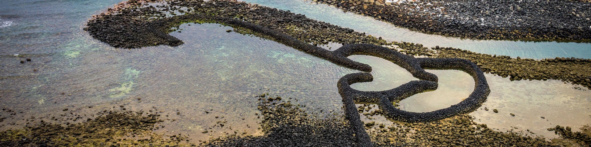 A rocky shoreline with clear water and a bicycle wheel-like formation.