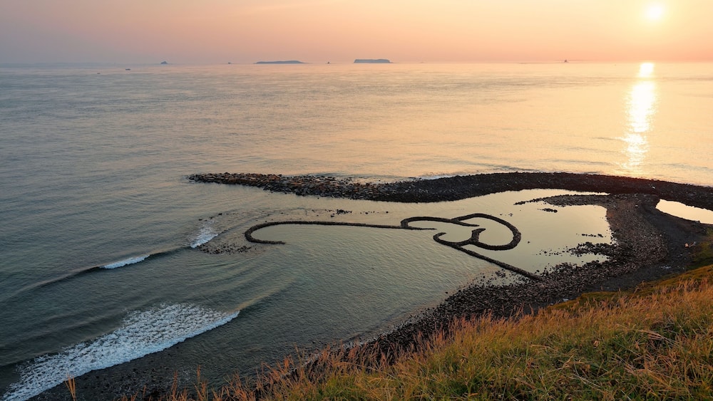 Sunrise over the Double-Heart Stacked Stones or Twin-Heart Fish Trap, which is a fishing weir and a popular tourist attraction in Cimei, Penghu, Taiwan, with golden sunlight reflected in the seawater