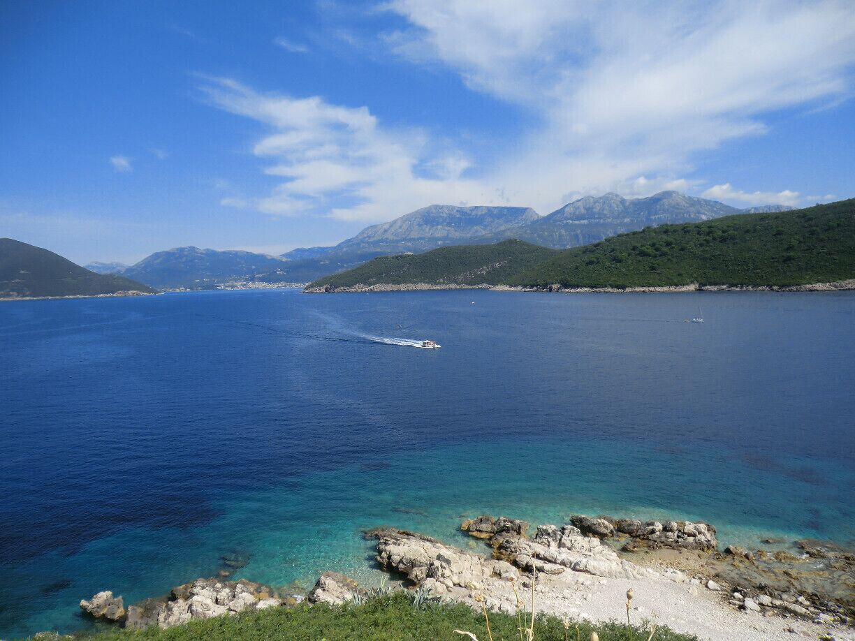 A coastal landscape with clear blue waters, rocky shorelines, and distant mountains under a clear sky.
