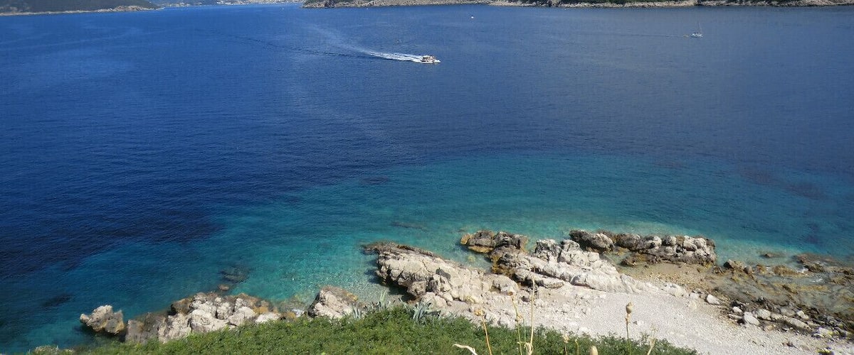 A coastal landscape with clear blue waters, rocky shorelines, and distant mountains under a clear sky.