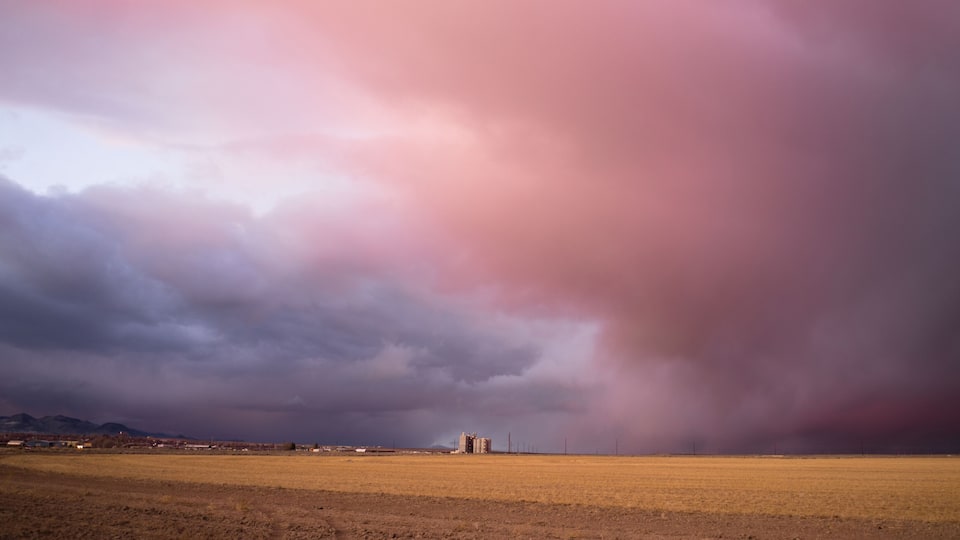 A stormy landscape with a field and distant buildings.