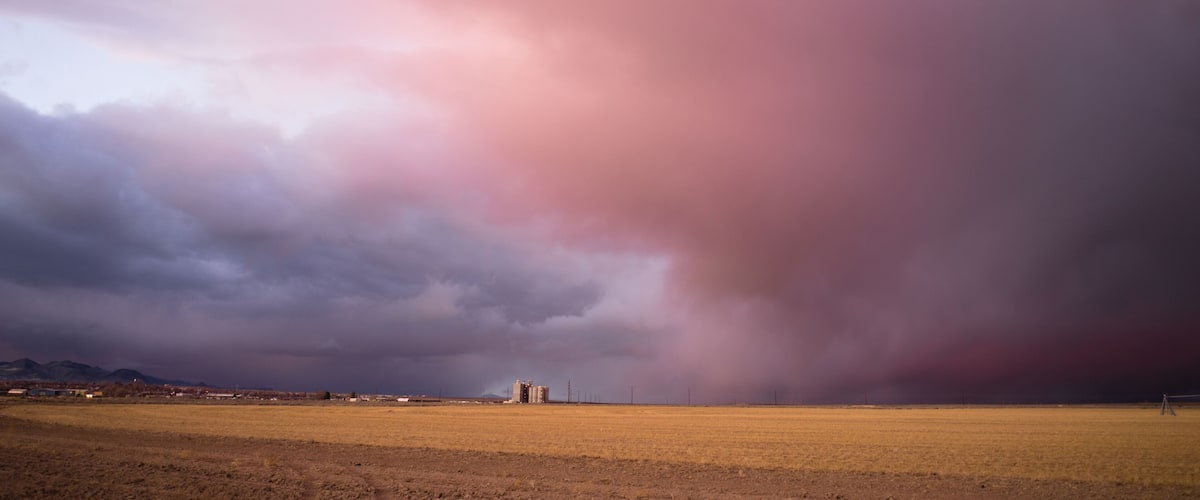 A stormy landscape with a field and distant buildings.