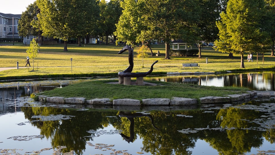 A park with a pond, a sculpture, and trees.