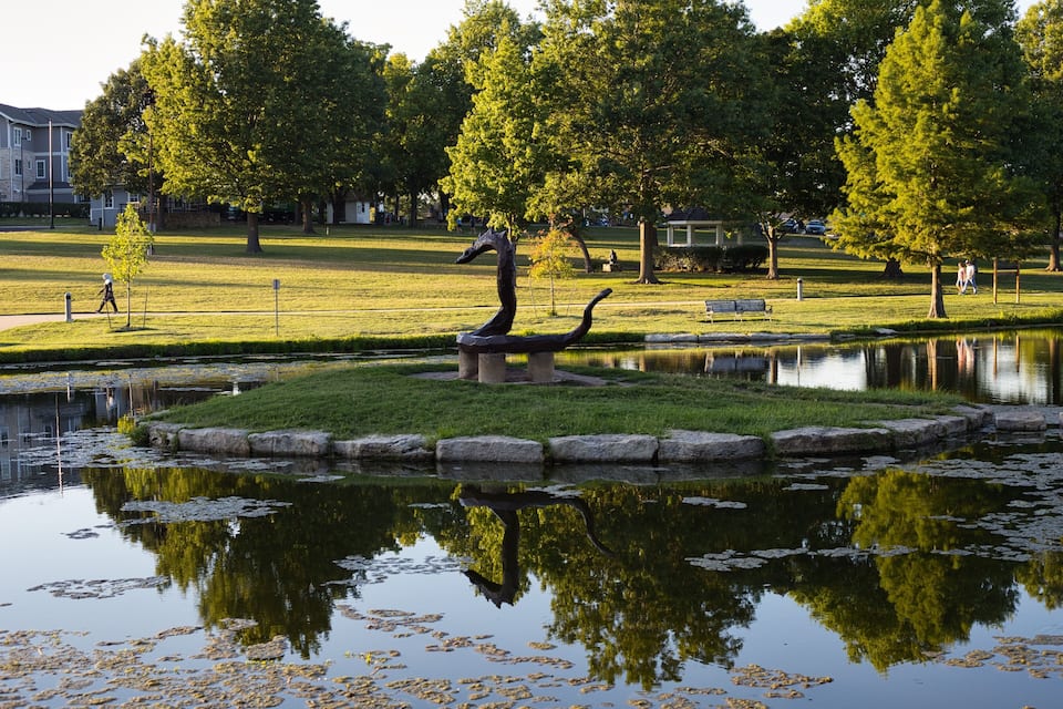 Ein Park mit Teich, Skulptur und Bäumen.