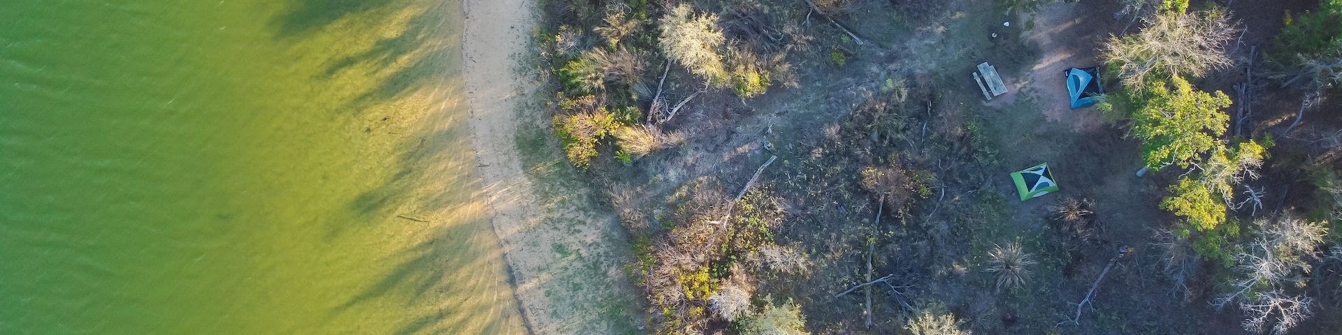 An aerial view of a coastal area with a sandy beach, dense vegetation, and three tents.