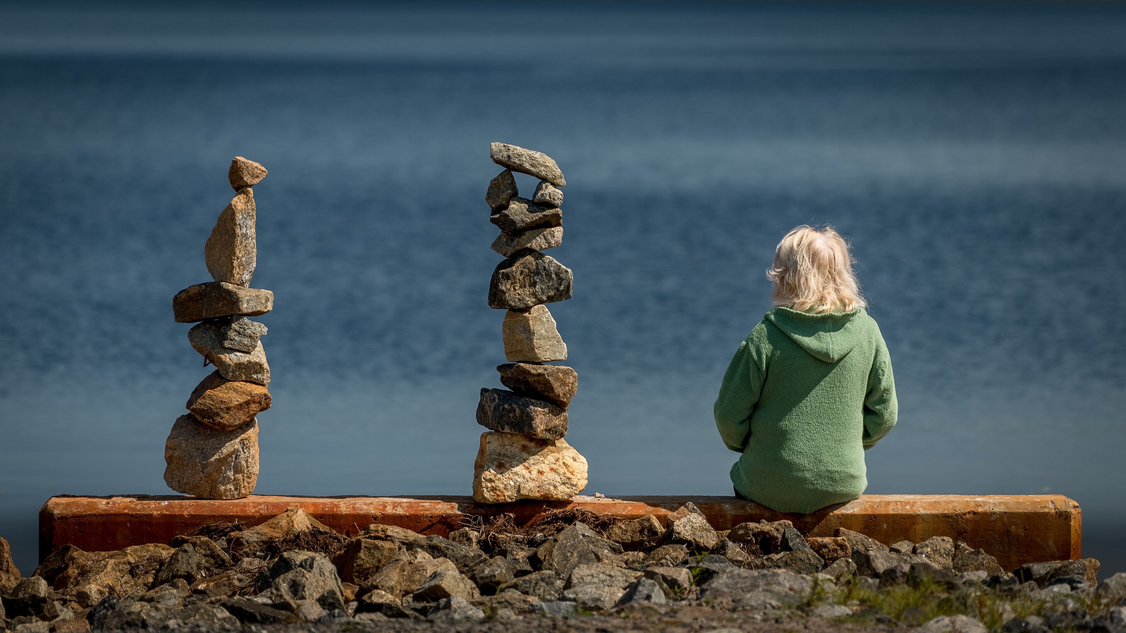 A woman sitting along side two balanced rock piles (cairns) along the shore of Tupper Lake in the Adirondacks, New York
