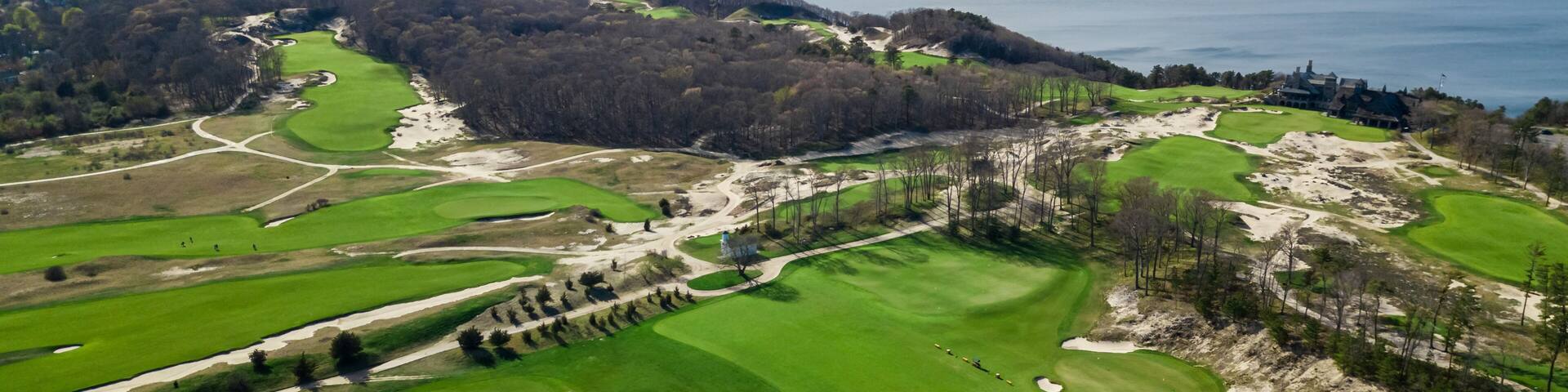 A golf course with sand bunkers, a clubhouse, and a view of the ocean.