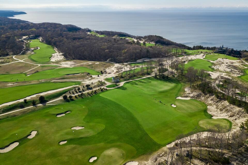 A golf course with sand bunkers, a clubhouse, and a view of the ocean.