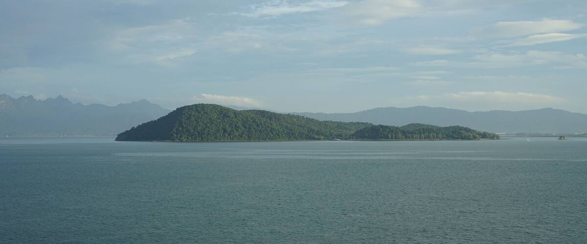 A calm body of water with a small island covered in greenery in the distance.