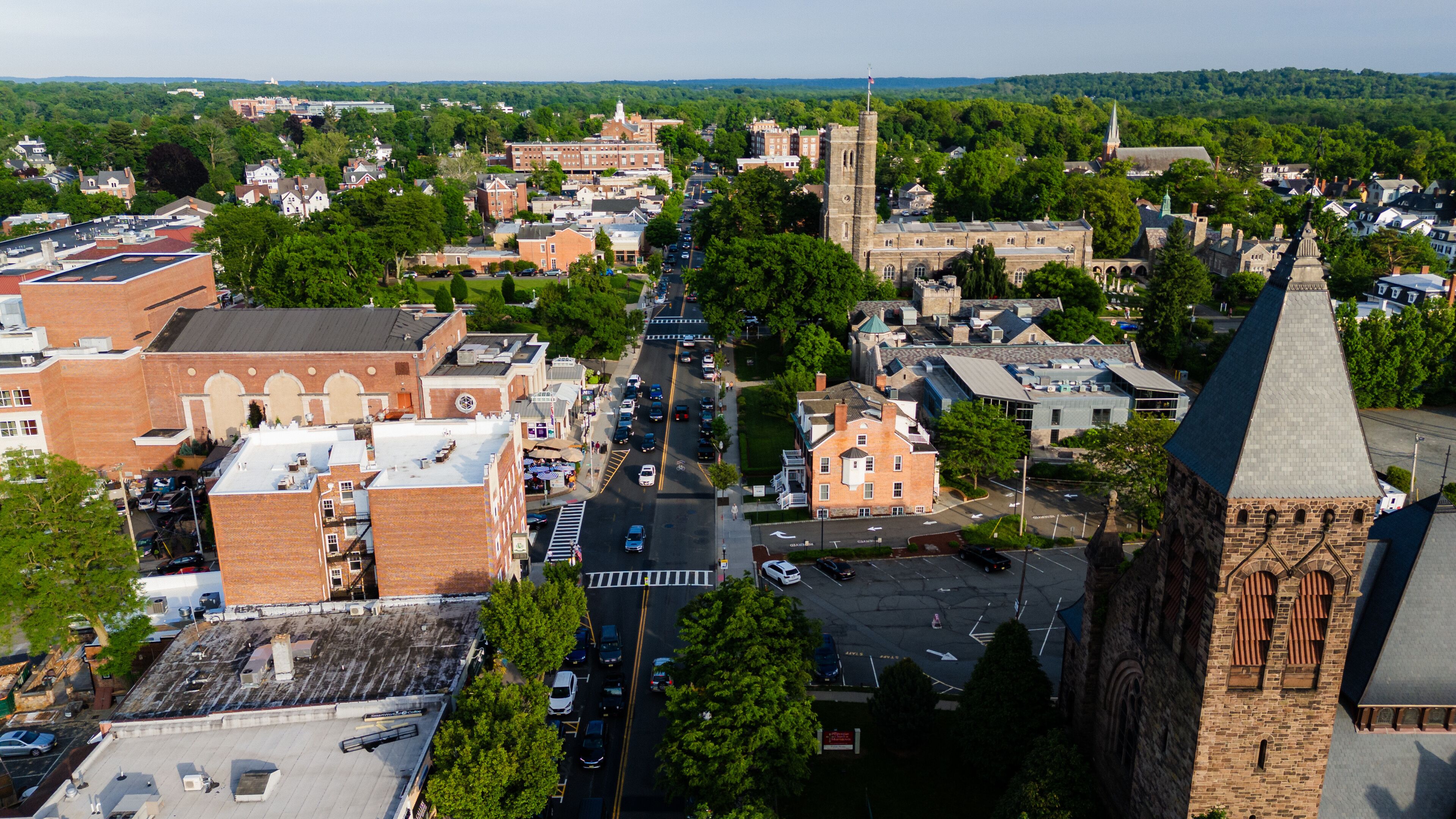 A town with a prominent church steeple, a central road, and surrounding greenery.