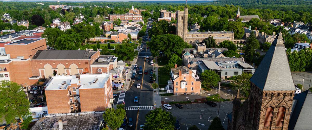 A town with a prominent church steeple, a central road, and surrounding greenery.