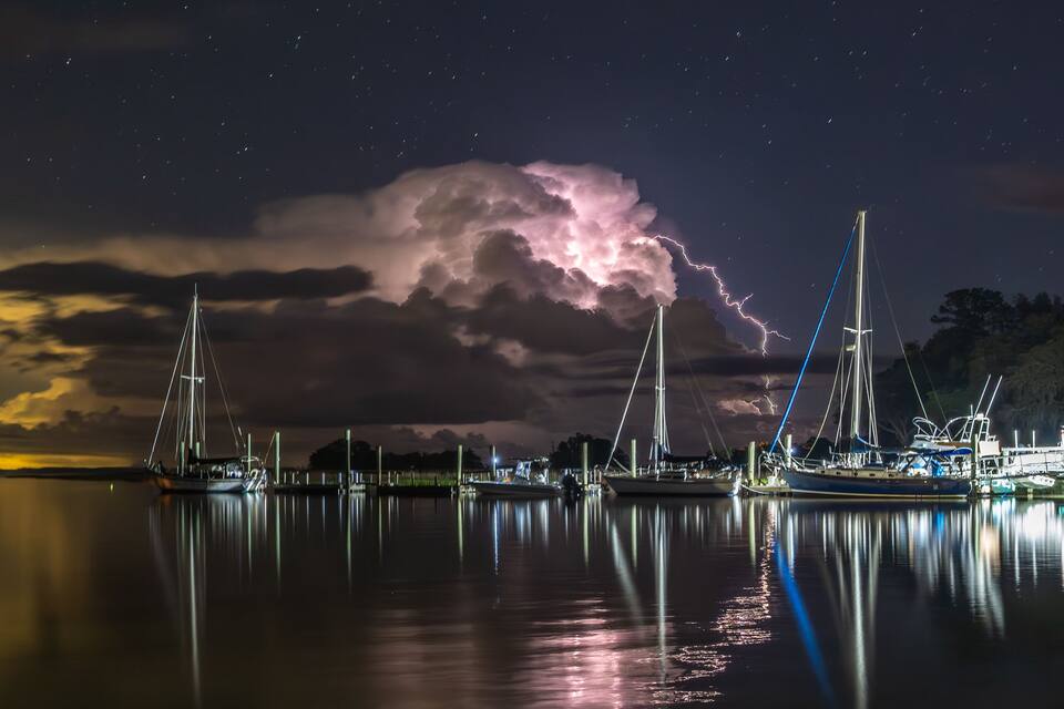 A marina at night with boats docked, a stormy sky, and lightning.