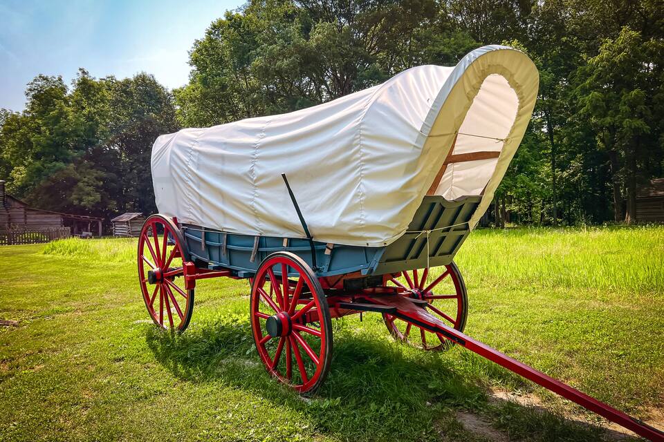 A covered wagon with red wheels parked on a grassy field.