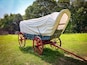 Rear view of a 19th century style horse-drawn carriage or covered wagon set against a green rural nature background.