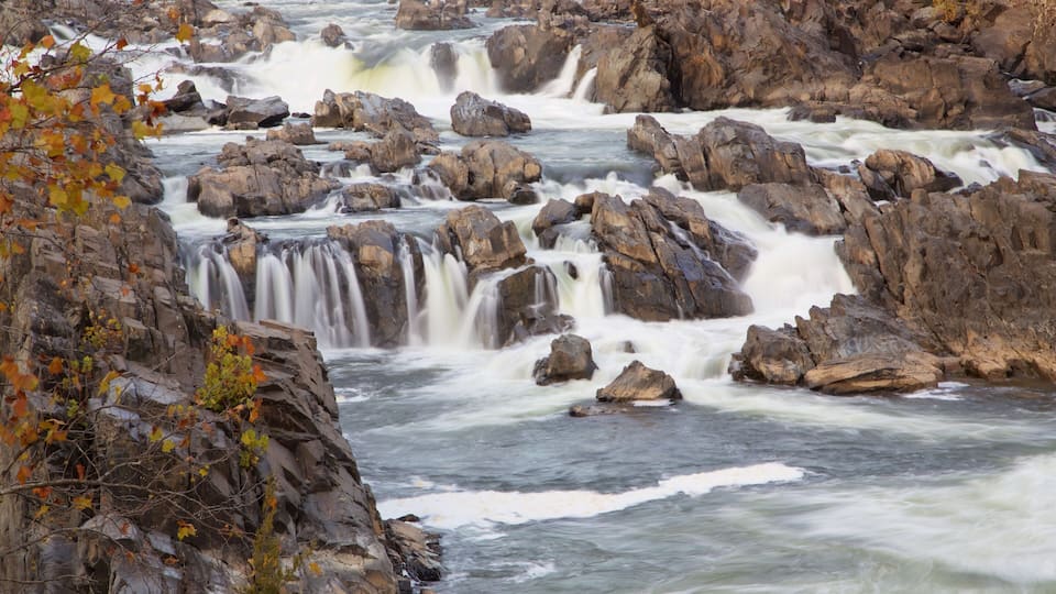 A river with multiple waterfalls surrounded by rocky terrain and autumn foliage.