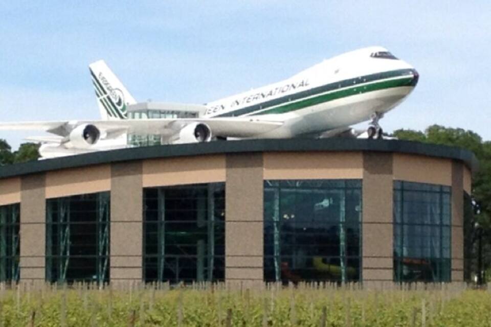 Un grand avion est garé sur le toit d’un bâtiment, avec un vignoble en premier plan.