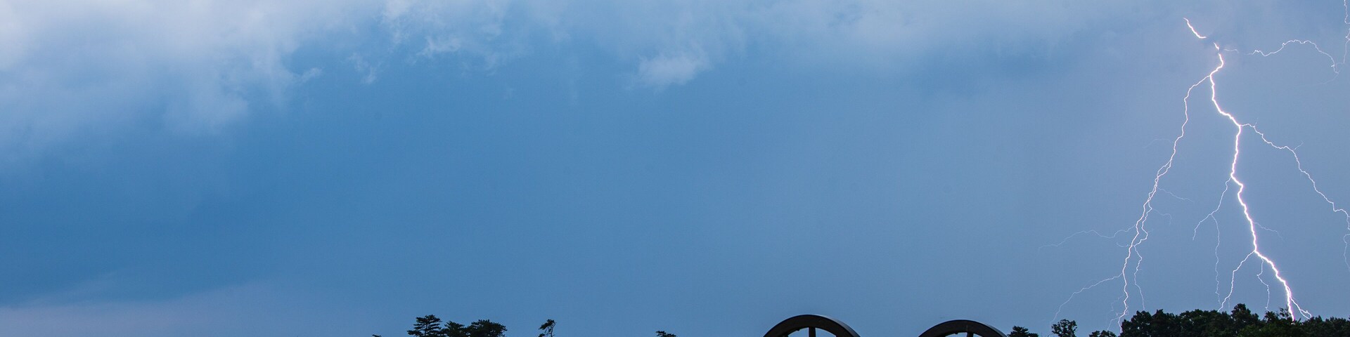 A cannon in a field with a stormy sky and lightning.
