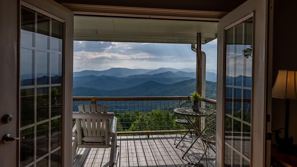 A wooden deck with a white chair and a small table, overlooking a mountain range.