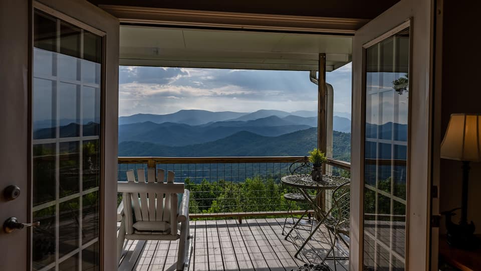 A wooden deck with a white chair and a small table, overlooking a mountain range.
