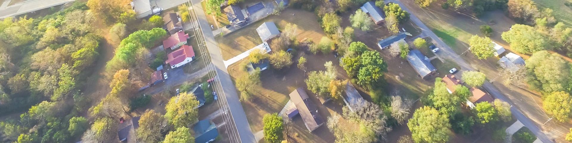 Panorama scenic aerial green suburban area of Ozark, Arkansas, USA. Overhead residential neighborhood tightly packed homes, driveway surround lush tree flyover in autumn sunset. View from East side