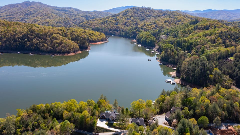 A lake surrounded by forested hills, boats on the water, and houses near the shore.