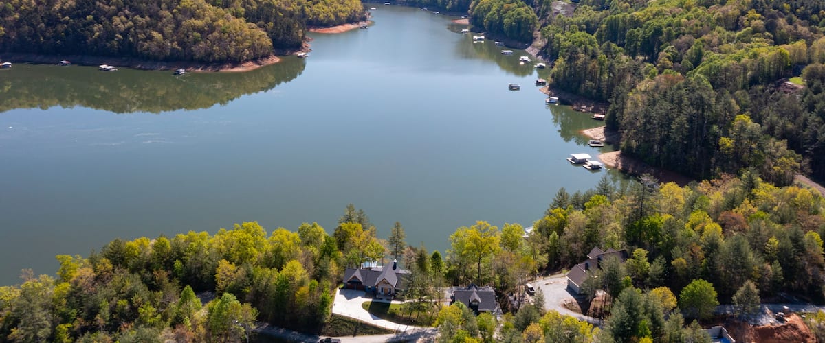 A lake surrounded by forested hills, boats on the water, and houses near the shore.