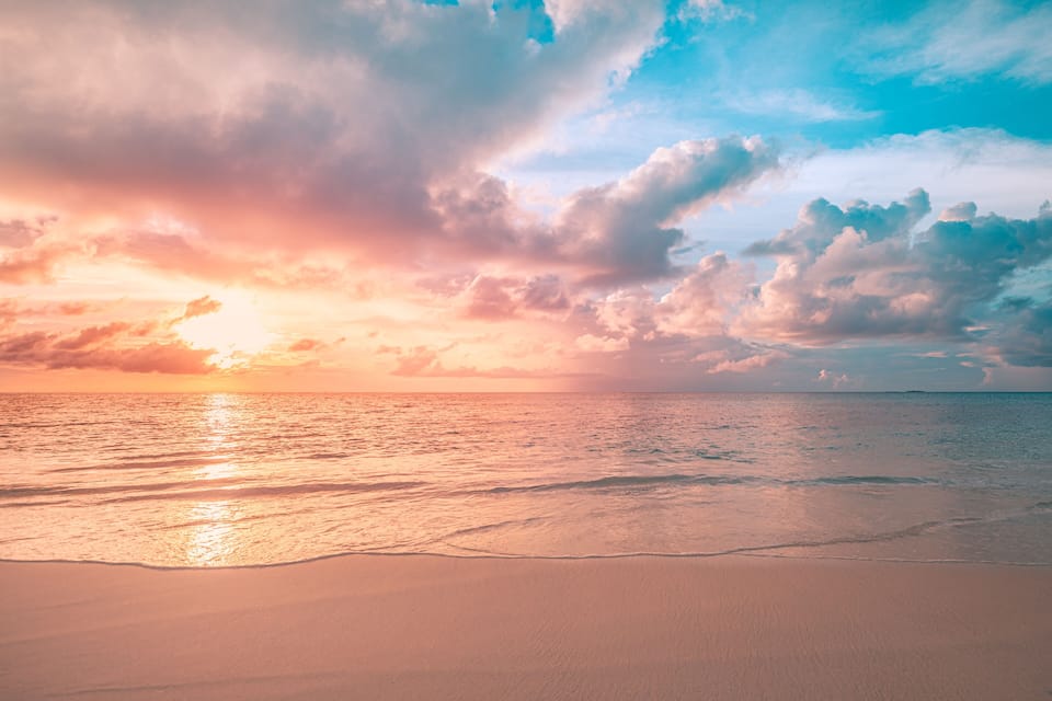 A beach with a sunset, ocean waves, and clouds.