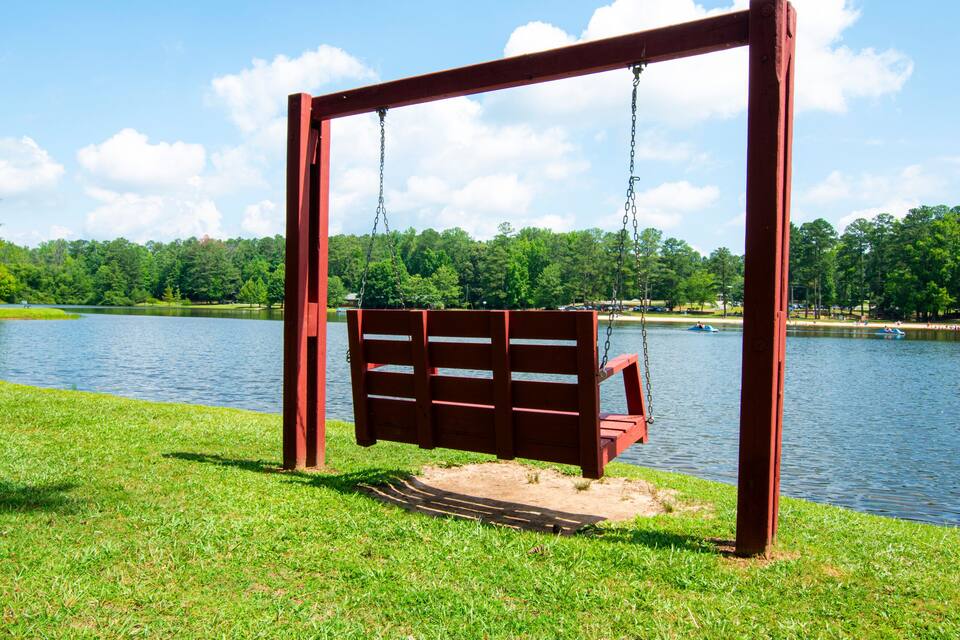 A wooden swing set by a lake with a clear sky.