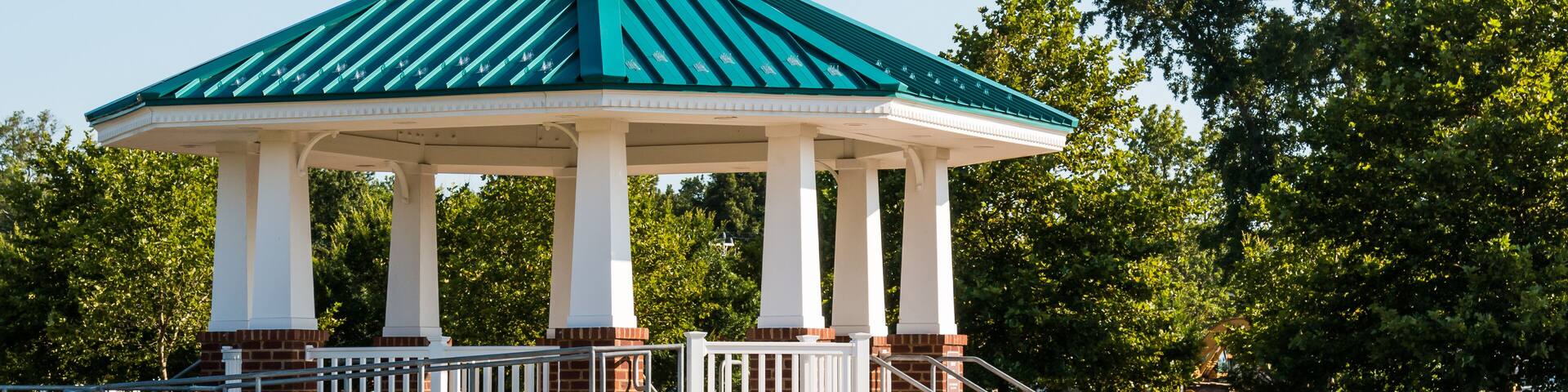 A gazebo with a green roof and white columns in a park.