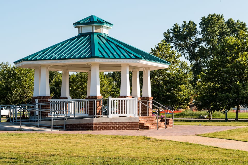A gazebo with a green roof and white columns in a park.